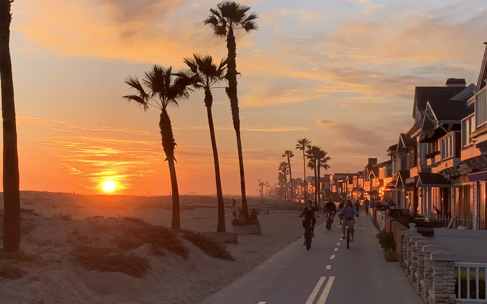 Bicycles on the Balboa Peninsula oceanfront boardwalk in Newport Beach, with palm trees, the beach, and the Newport Pier